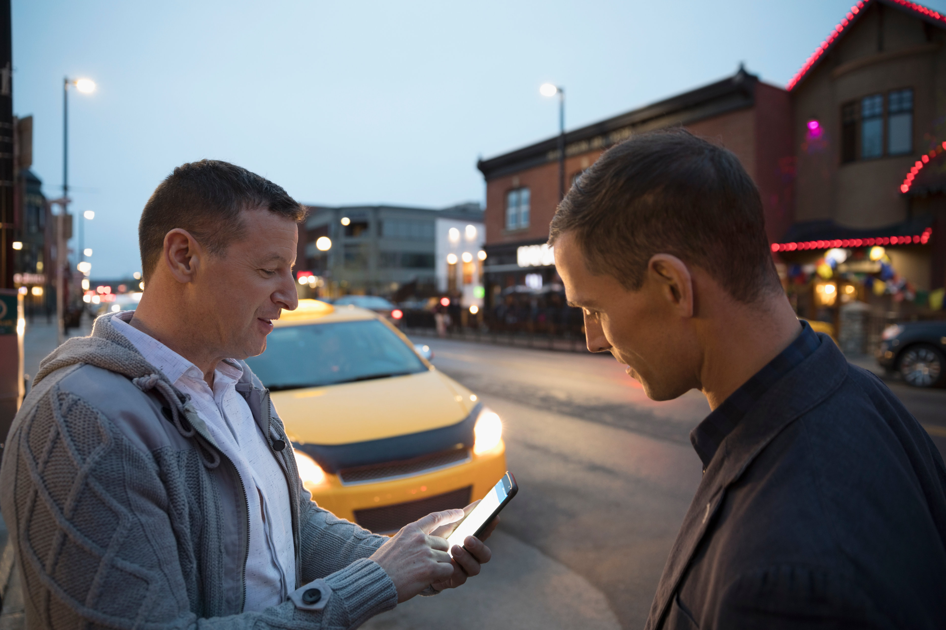 Men using smartphone for crowdsourced taxi on urban street at night
